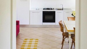 A kitchen with white cabinets, a gas stove, and a sink. There is a checkered mat on the floor and a dining table with chairs. - Apartment in Golfo Aranci With Terrace (Arzachena)