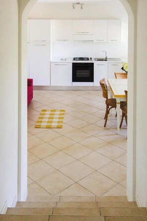 A kitchen with white cabinets, a stove, and a dining area with a table and chairs. - Apartment in Golfo Aranci With Terrace (Arzachena)