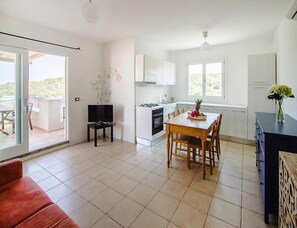 A modern kitchen with white cabinets, a dining table with chairs, a TV on a stand, and a balcony with a view. - Apartment in Golfo Aranci With Terrace (Arzachena)