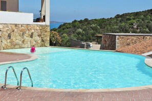 A swimming pool with stone walls, a clear view of the sea, and a hilly landscape in the background. - Apartment in Golfo Aranci With Terrace (Arzachena)