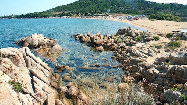 A rocky shoreline with clear water, a sandy beach, and a hill in the background. - Apartment in Golfo Aranci With Terrace (Arzachena)