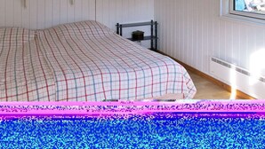 A bedroom with a bed, a shelf with decorative items, a window with a view, and a radiator. - Apartment in Golfo Aranci With Terrace (Arzachena)