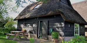 Ein rustikales Haus mit Strohdach, Holzfassade und einer kleinen Veranda mit Tisch und Stühlen.