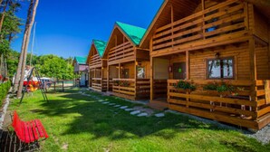 A row of wooden cabins with green roofs, arranged in a row with a grassy area in front. - Year-round Holiday House With a Terrace, Near the Sea, Pustkowo (Rewal)