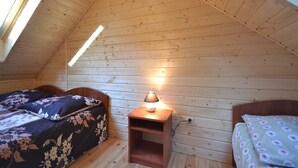 A cozy attic bedroom with wooden walls, a slanted ceiling, and a skylight. There are two beds with floral bedding, a bedside table with a lamp, and a small shelf. - Year-round Holiday House With a Terrace, Near the Sea, Pustkowo (Rewal)