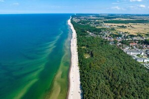 An aerial view of a coastal area with a long beach, dense forest, and residential buildings. - Year-round Holiday House With a Terrace, Near the Sea, Pustkowo (Rewal)