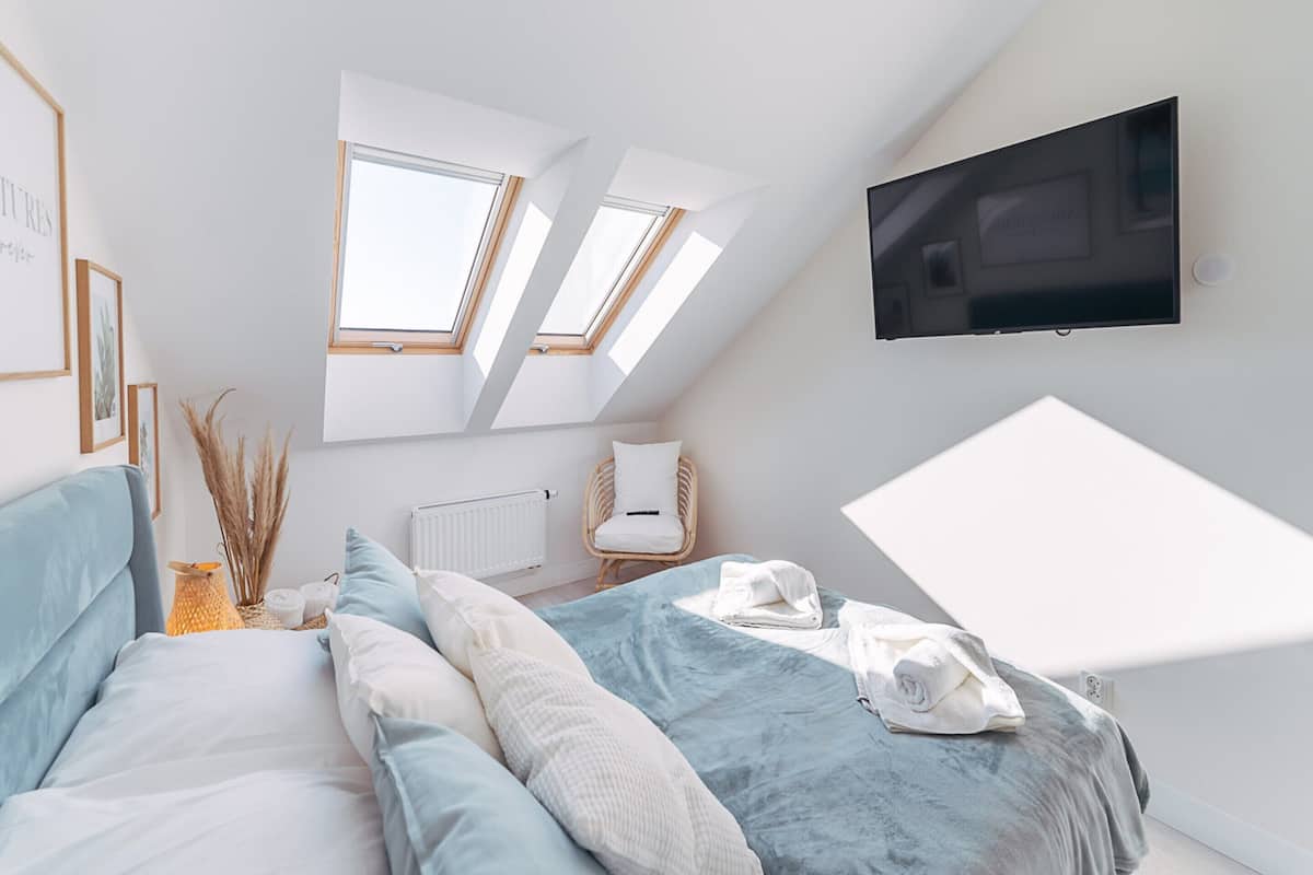 Ein modernes Schlafzimmer mit Bett, Dachfenstern, Fernseher und Heizkörper.