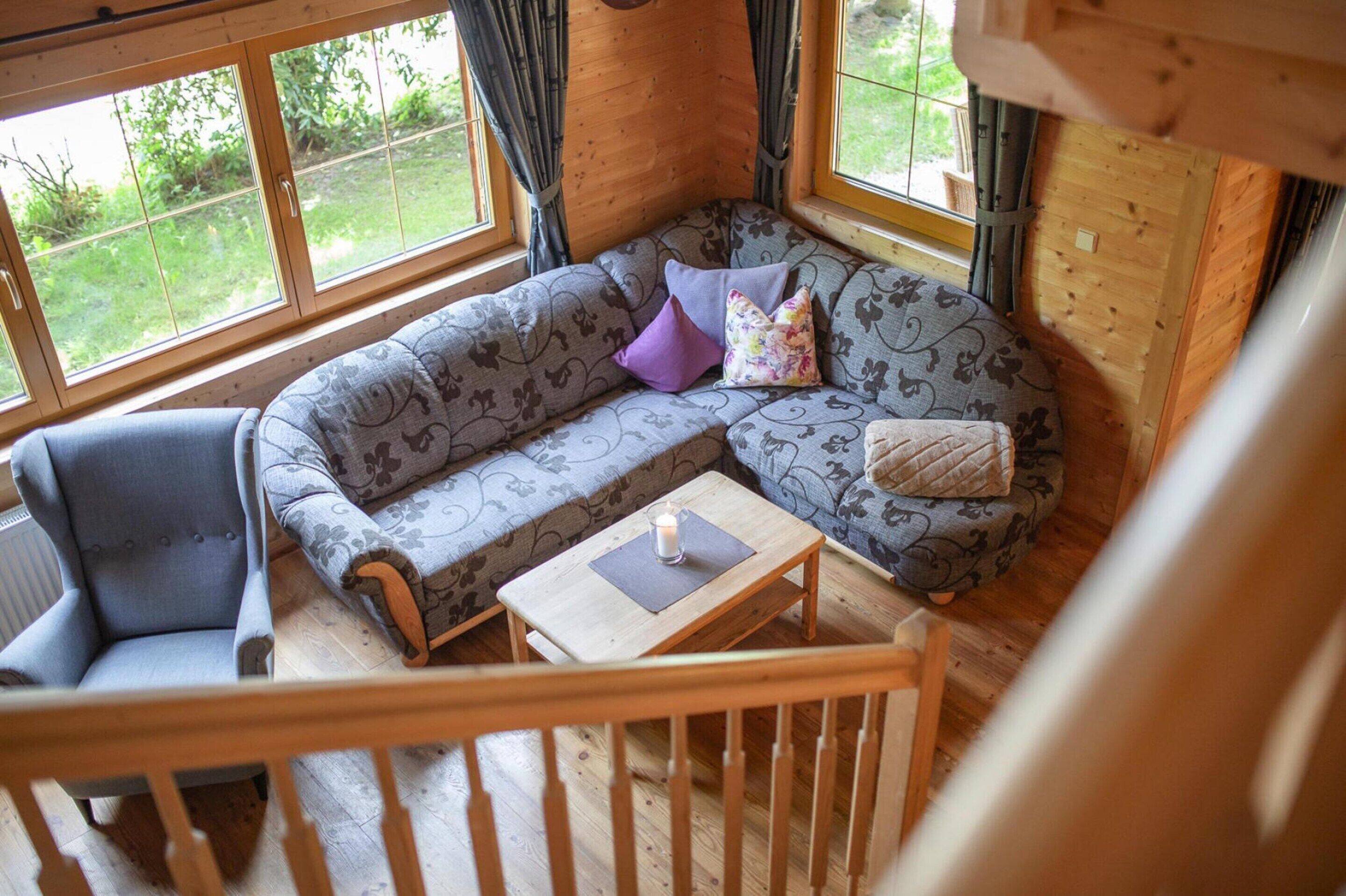 A cozy cabin interior with a sofa, a chair, a small table, and a window with curtains.