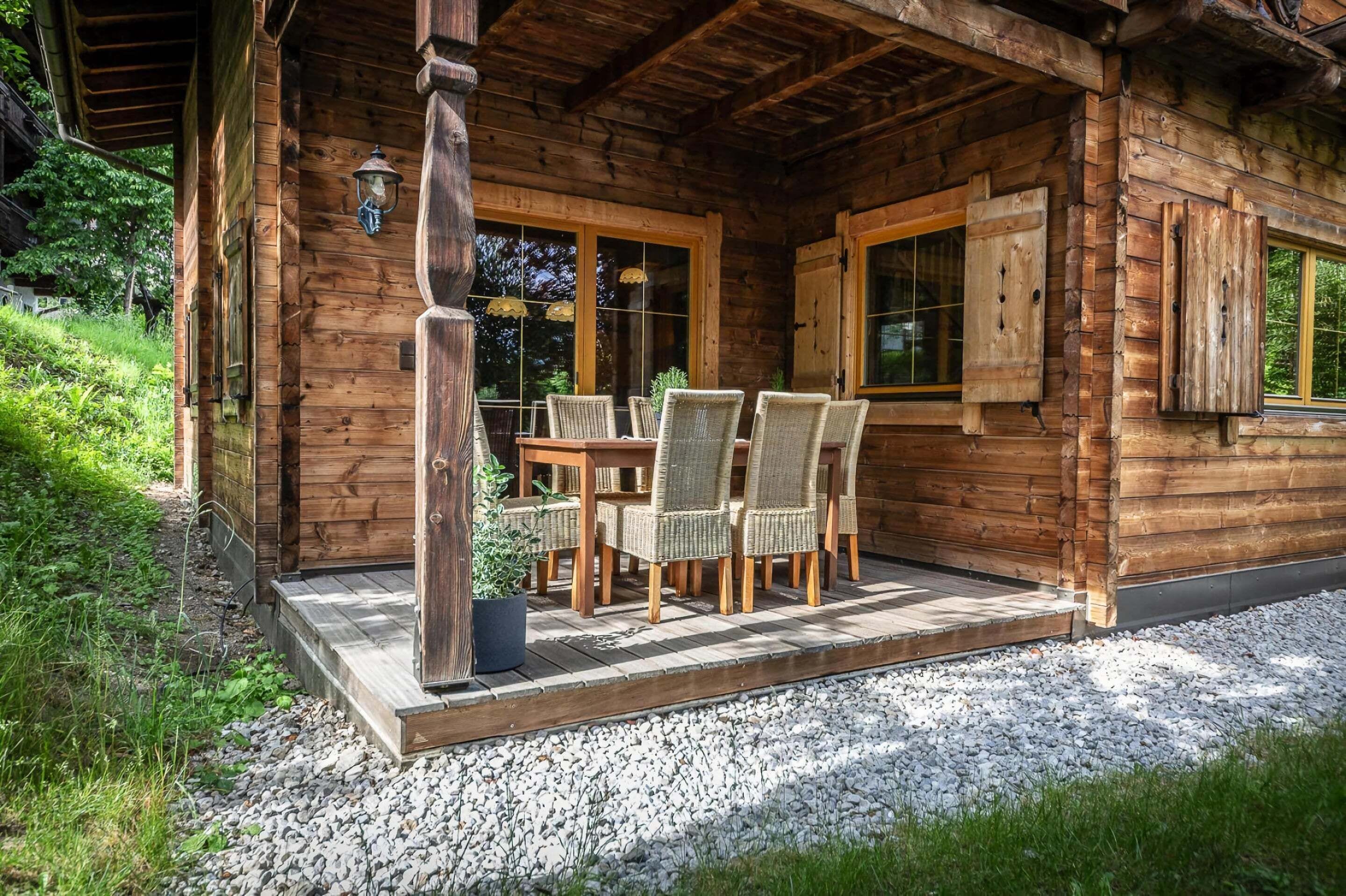 Een houten chalet met een overdekte veranda, rieten stoelen en een tafel.