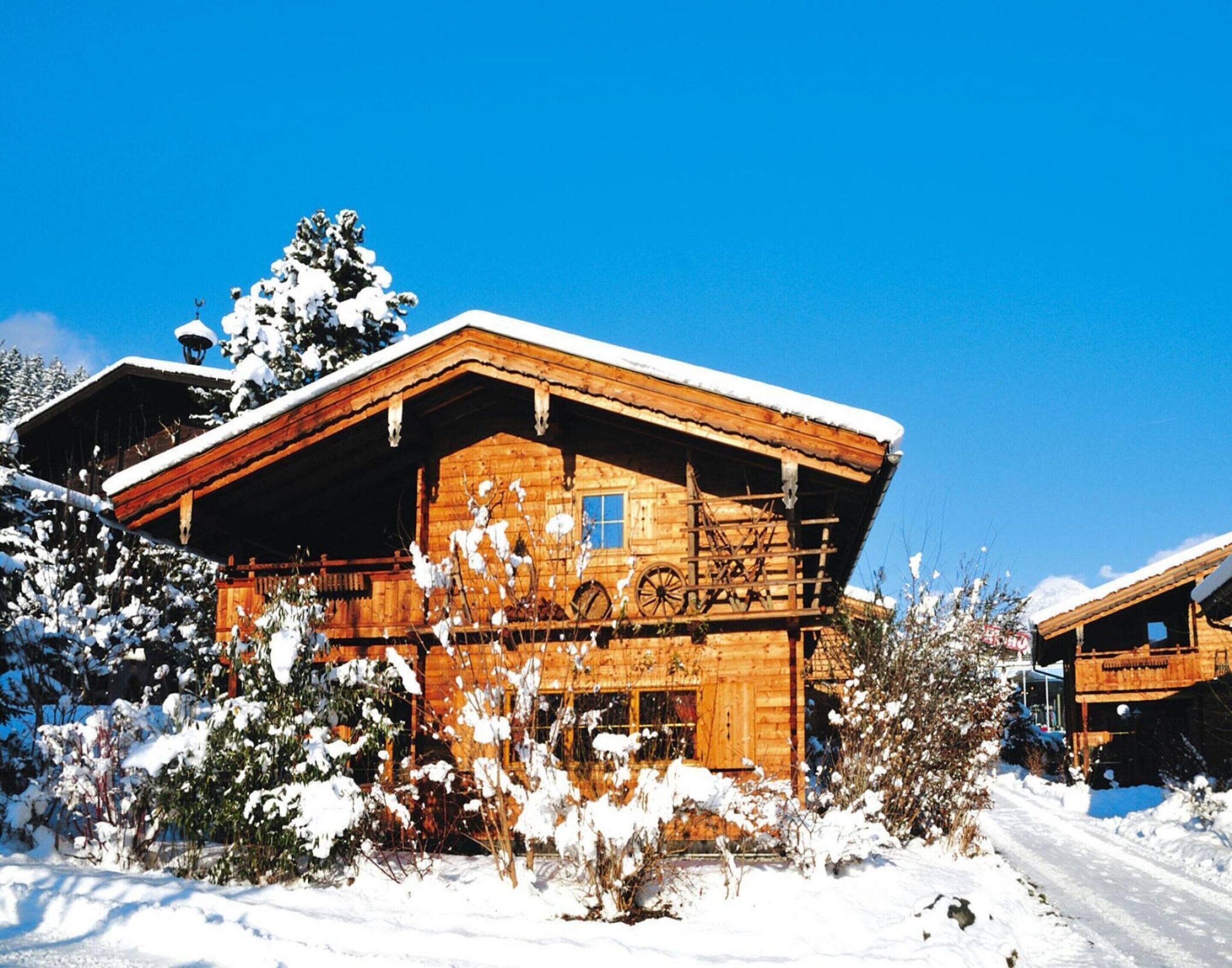 Uma cabana de madeira com telhado coberto de neve, rodeada por vegetação também coberta de neve.