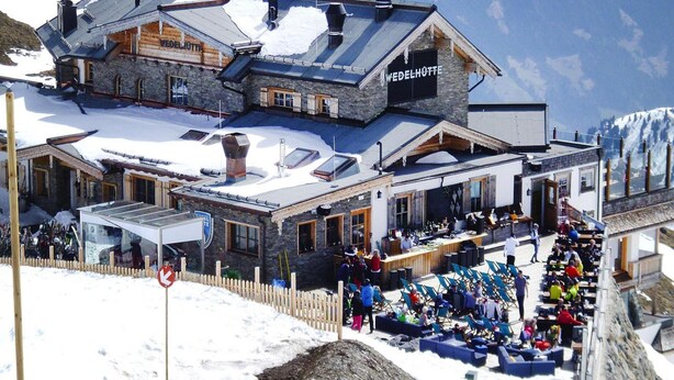 A mountain lodge with a stone facade, wooden balconies, and a sign reading "WEDELHÜTTE". - Chalets Almdorf Zillertal, Fugen (Fuegen)