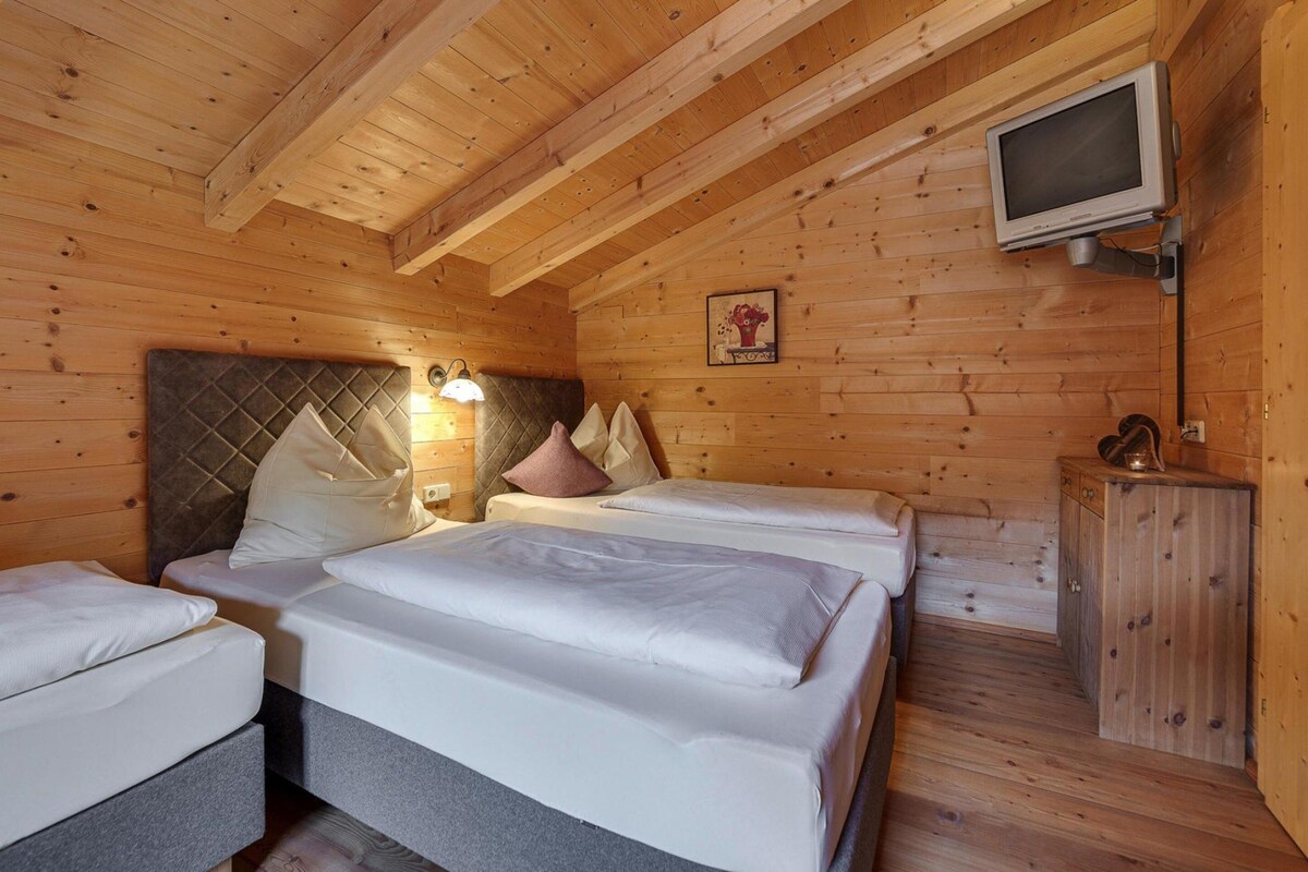 A wooden cabin room with two beds, a television, and a cabinet.