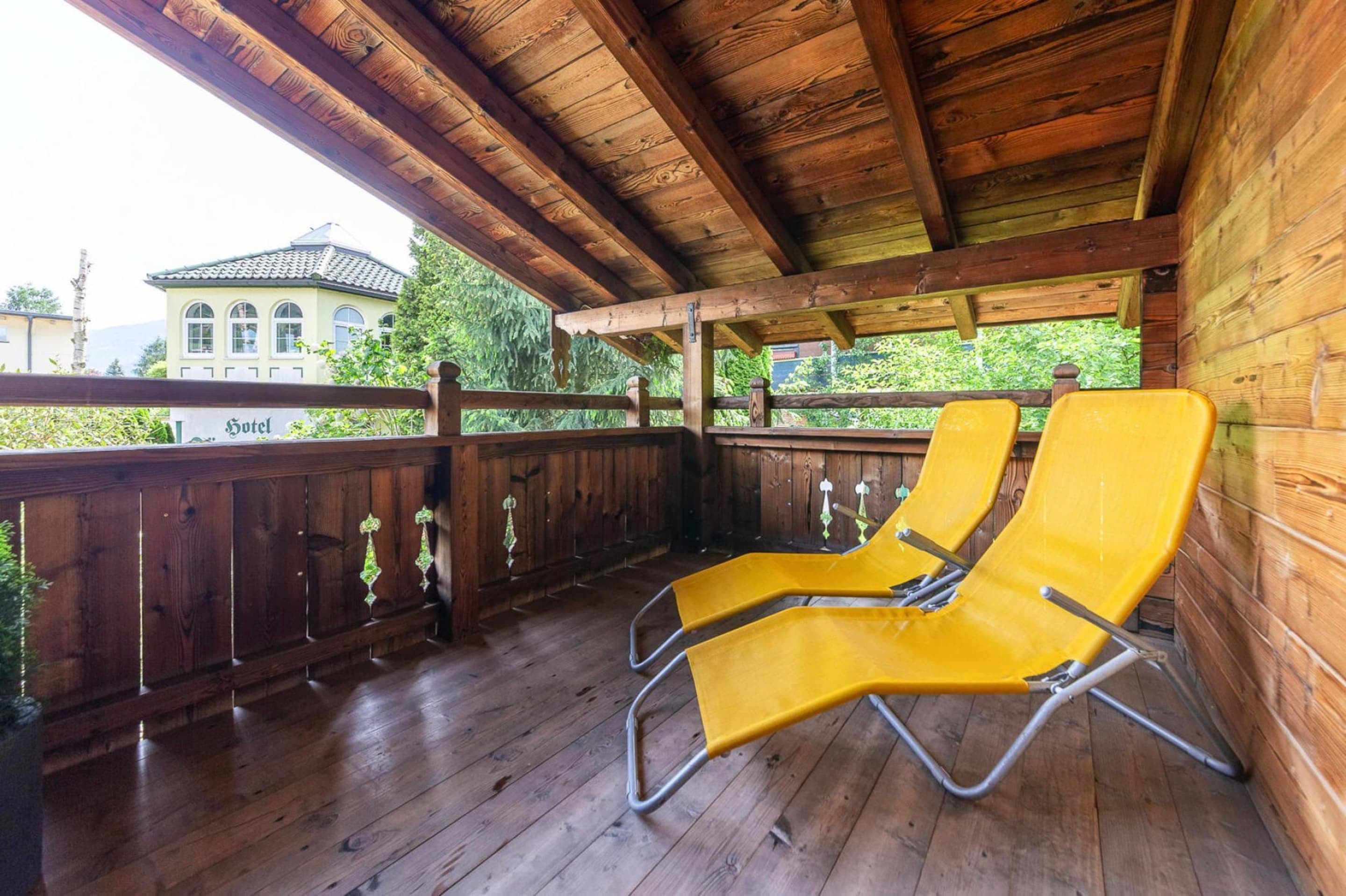 A wooden deck with two yellow lounge chairs, a wooden railing, and a view of a building labeled "Hotel" in the background.