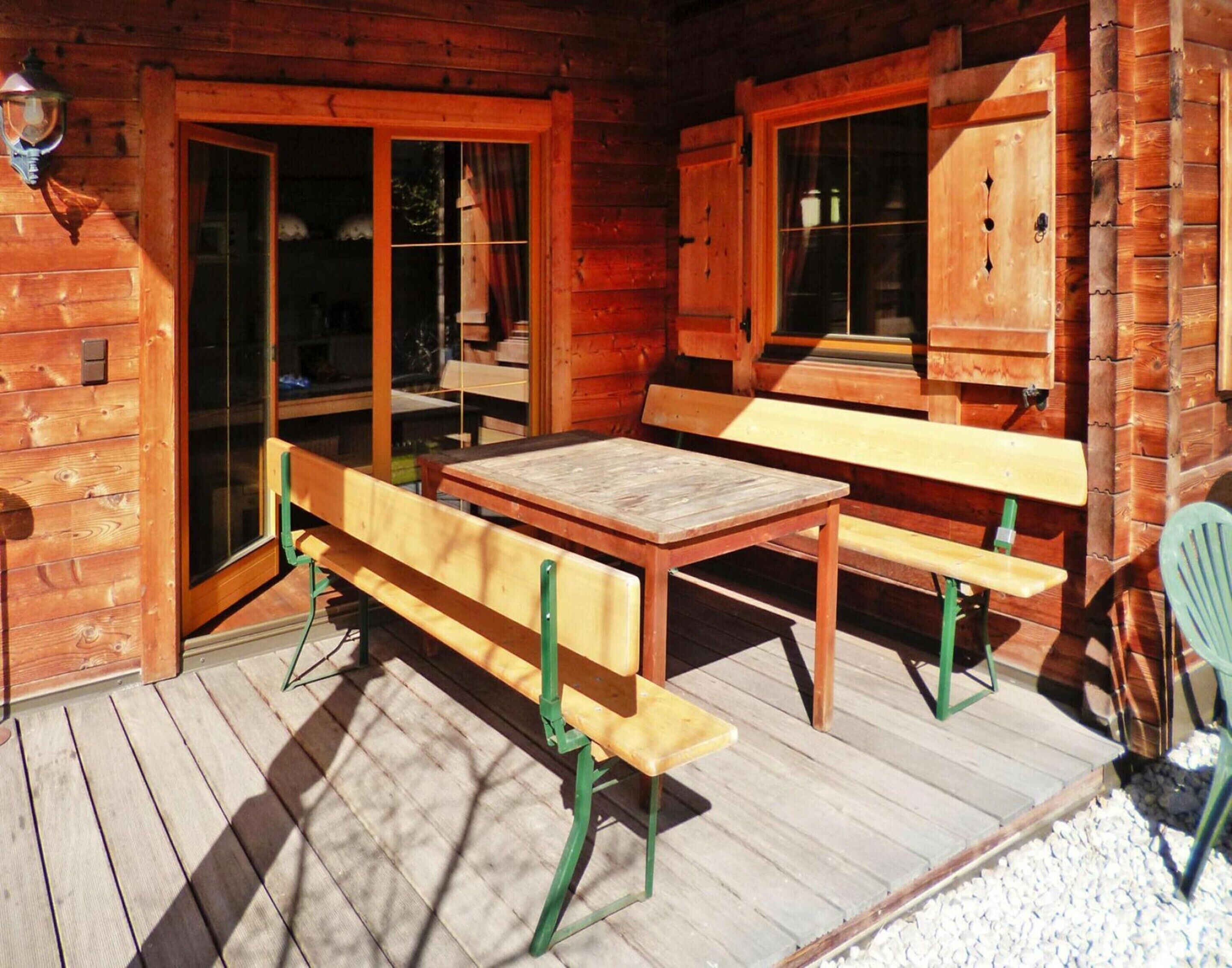 En stuga av trä med en veranda, komplett med ett träbord och bänkar, samt ett fönster med utsikt.