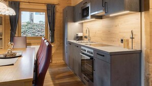 A modern kitchen with wooden cabinetry, stainless steel appliances, and a dining area with a table and chairs. - Chalets Almdorf Zillertal, Fugen (Fuegen)