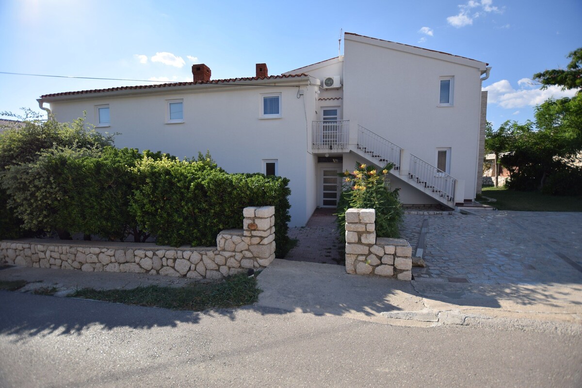 A two-story building with a stone wall entrance, a staircase, and a small balcony.