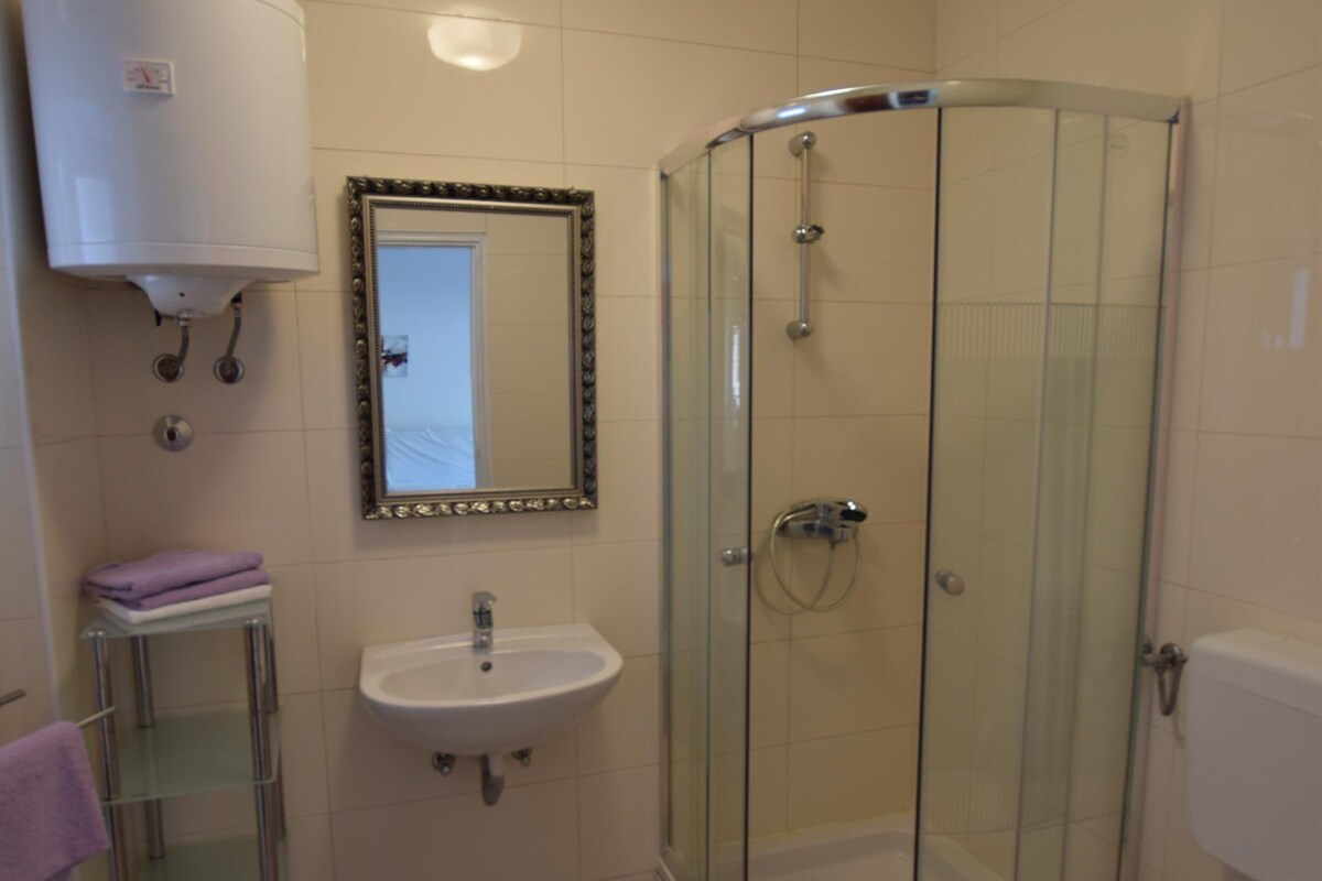 A bathroom with a glass-enclosed shower, a white sink, and a mirror with an ornate frame.