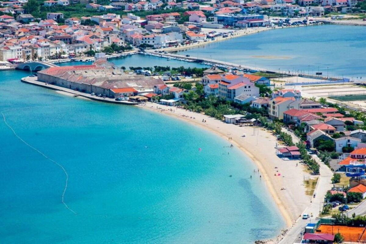 An aerial view of a coastal town with a beach, buildings, and a fortified structure.