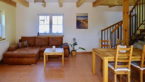 Una sala de estar con un sofá, una mesa de centro, una mesa de comedor con sillas, una escalera y una ventana.