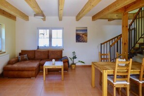 A living room with a sofa, a coffee table, a dining table with chairs, a staircase, and a window. - Farmstay Neuendorfkrug, Lutow (Luetow)