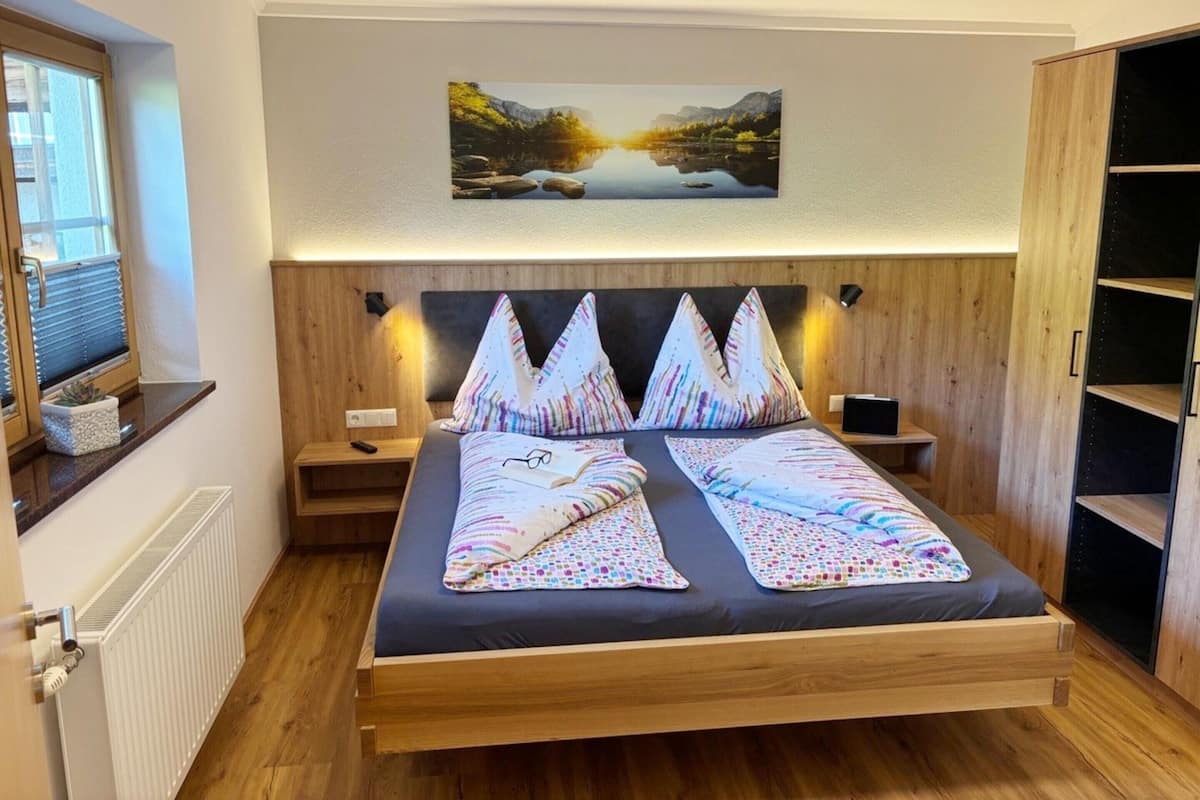 Ein modernes Schlafzimmer mit einem hölzernen Bett, einem Nachttisch, einem Wand-Fernseher und einem Bücherregal.
