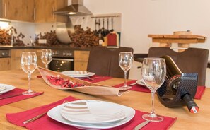 Een eettafel gedekt met borden, bestek en wijnglazen, met een fles wijn en een houten schaal met lekkernijen.