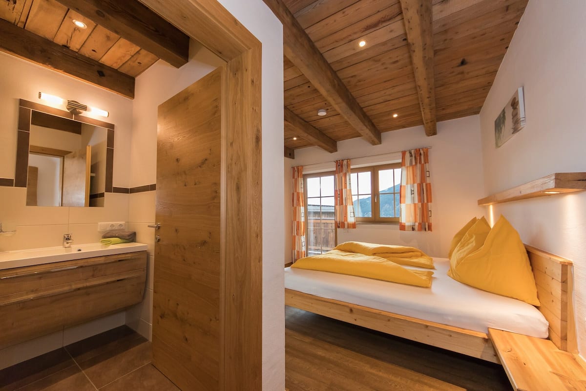 A bedroom with a wooden ceiling, a bed with yellow bedding, a wooden bedside table, and a window with curtains.