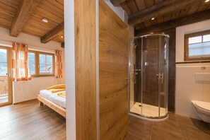 Een slaapkamer met een houten bed, een douchecabine van glas en uitzicht op bergen vanuit het raam.