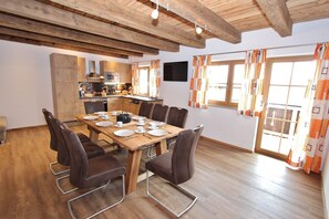 A dining area with a wooden table set for six, surrounded by six chairs. A kitchen with modern appliances is visible in the background. - Modern Mansion in Kaprun Near Ski Area (Kaprun)