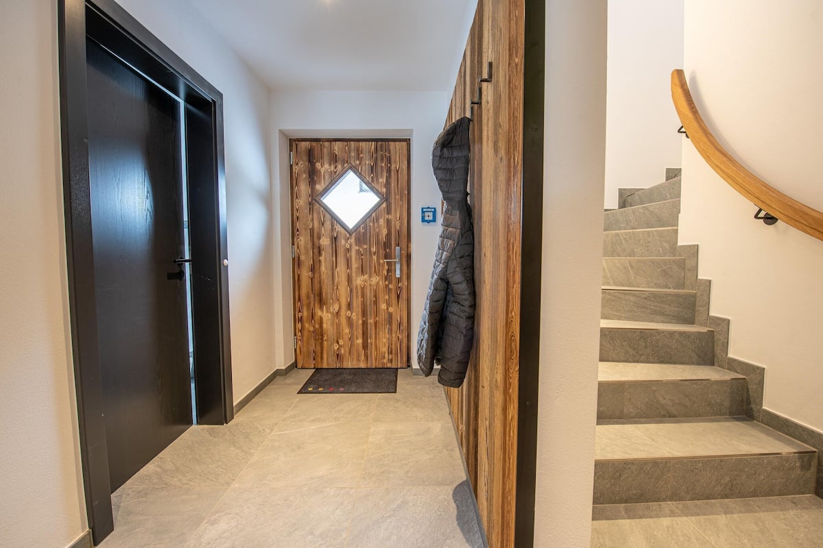 Un couloir avec une porte en bois, un manteau accroché au mur et un escalier.