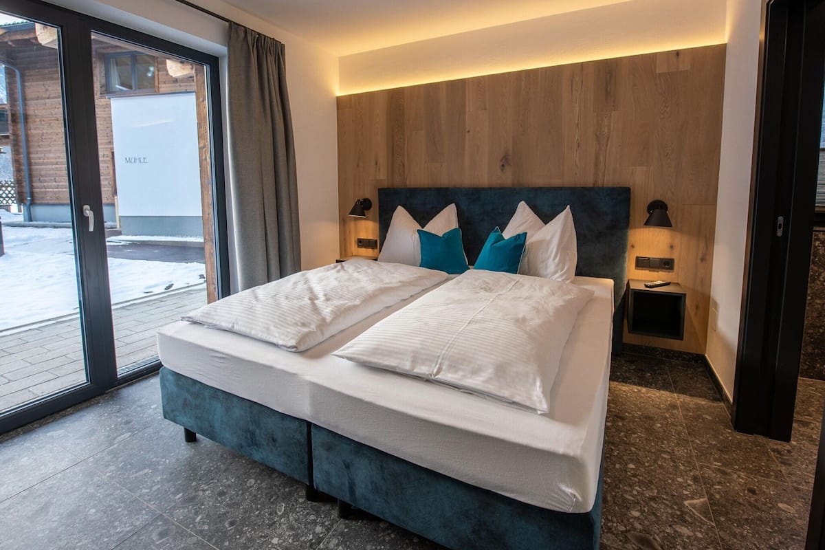 Une chambre d’hôtel moderne avec un lit double, une tête de lit en bois et une porte-fenêtre coulissante donnant sur un espace extérieur enneigé.