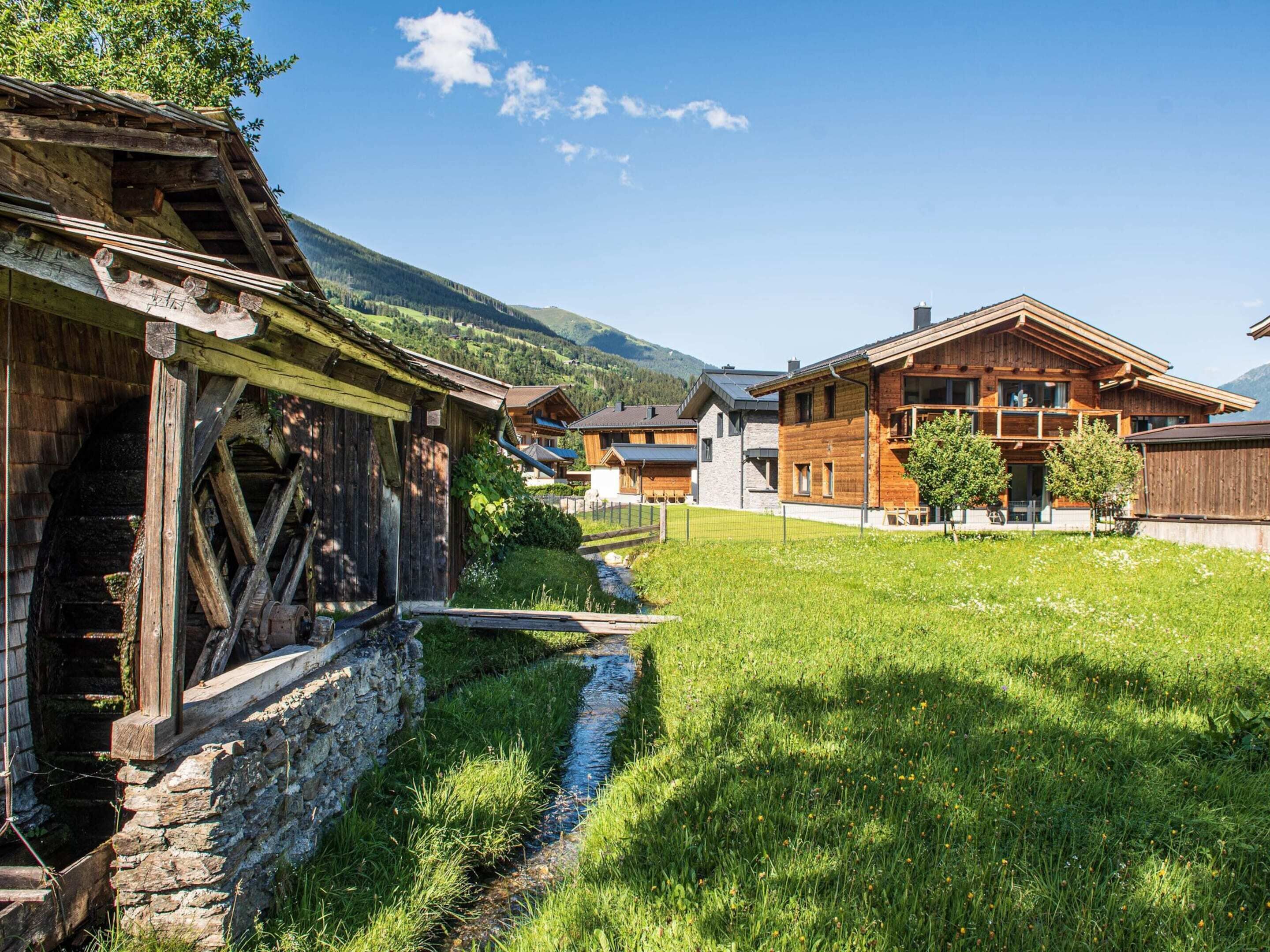 A traditional wooden house with a stone foundation, a wooden bridge, and a grassy area with a small stream.