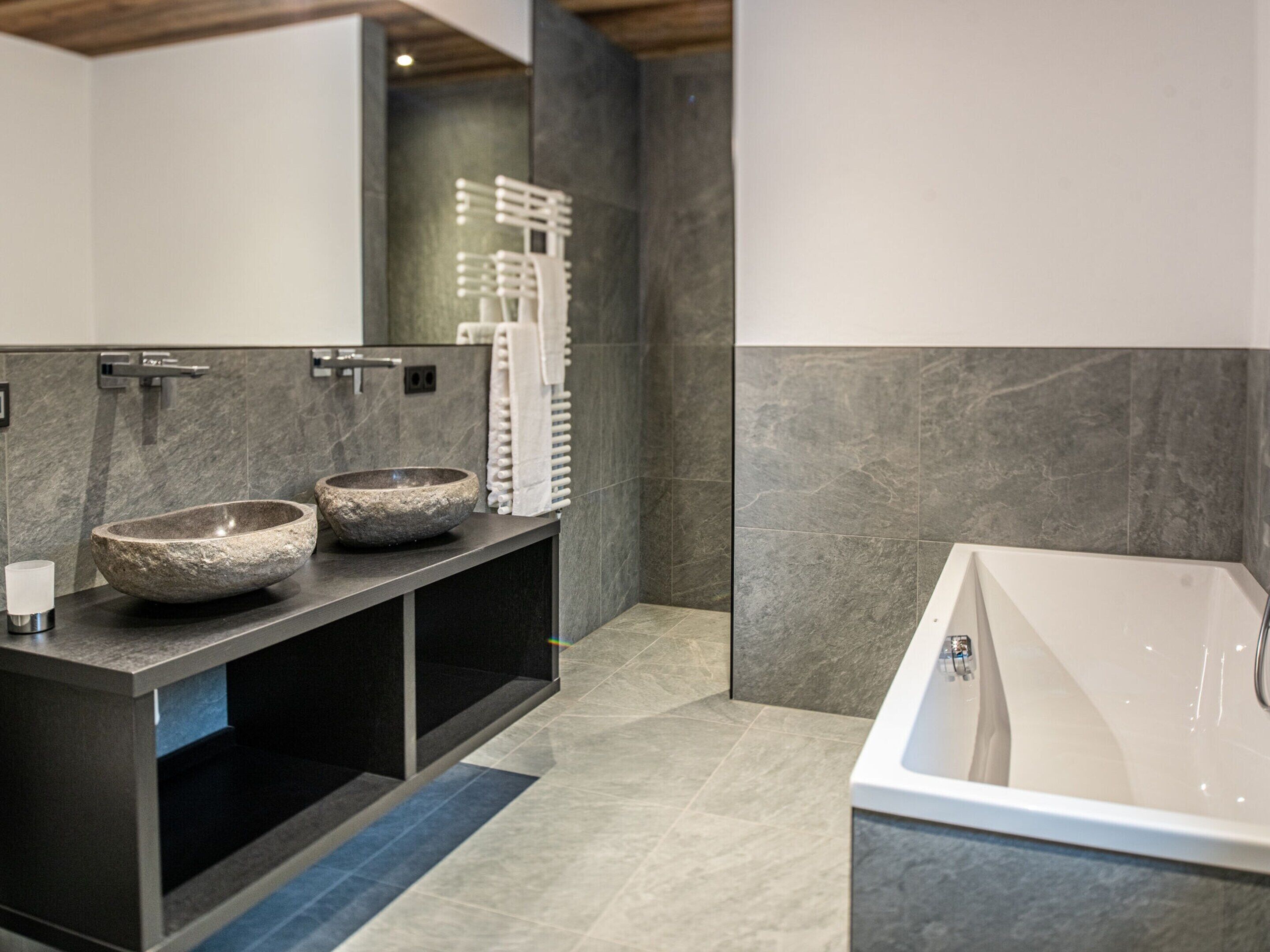 A modern bathroom with a large bathtub, two stone basins, and a towel rack.