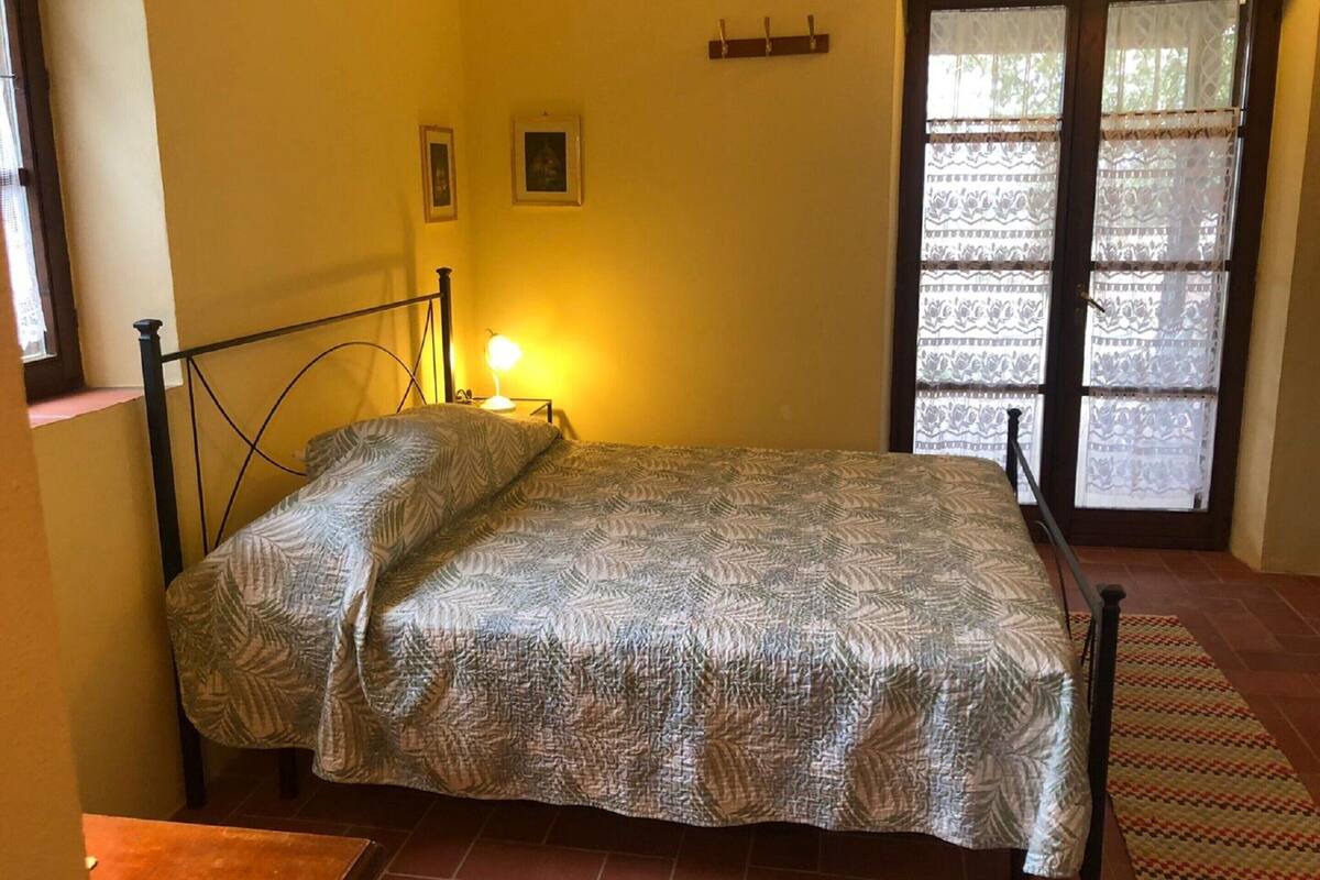 A single bed with a patterned bedspread in a room with yellow walls, a small bedside lamp, and a window with lace curtains.