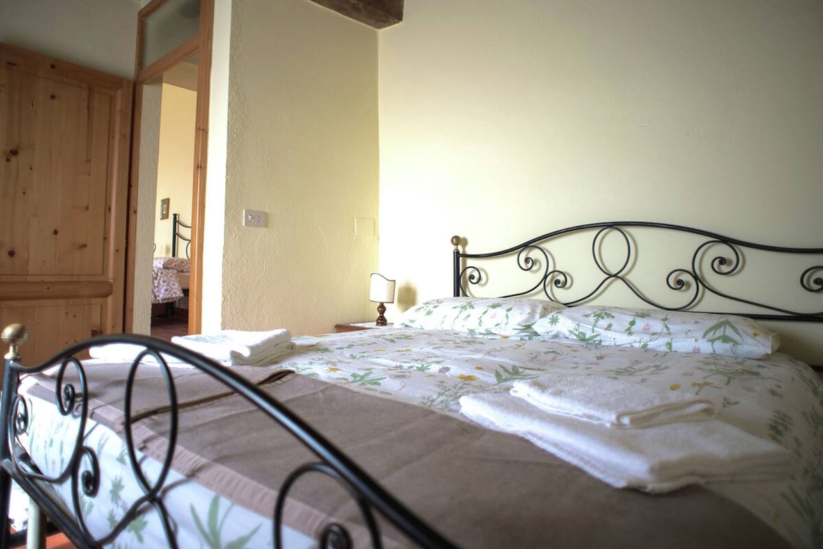 A bedroom with a bed, wooden door, and a small table with a lamp.