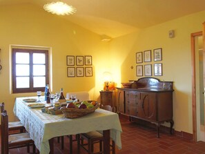 A dining area with a table set for four, a wooden cabinet, and a window with curtains. - Cozy Farmhouse in Paciano With Private Pool (Paciano)