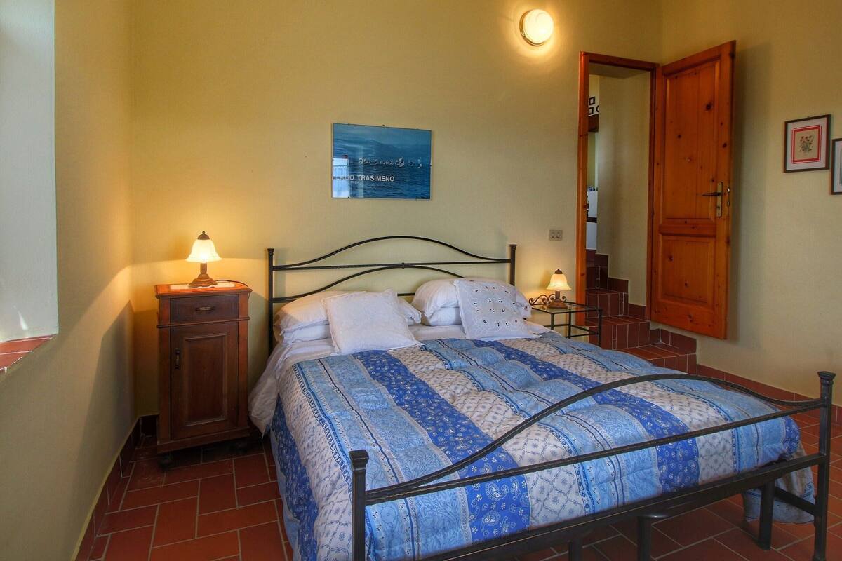 A bedroom with a bed, a nightstand, a lamp, a poster on the wall, and a wooden door.