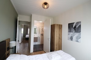 Une chambre d’hôtel avec un lit, une armoire en bois, un tableau accroché au mur, et une porte ouverte donnant sur une salle de bain et un espace douche.