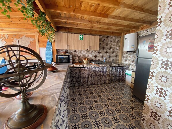 A kitchen with a wooden ceiling, patterned tiles, a microwave, a stove, and a refrigerator. - Aourir Waves Surf House (Aourir)