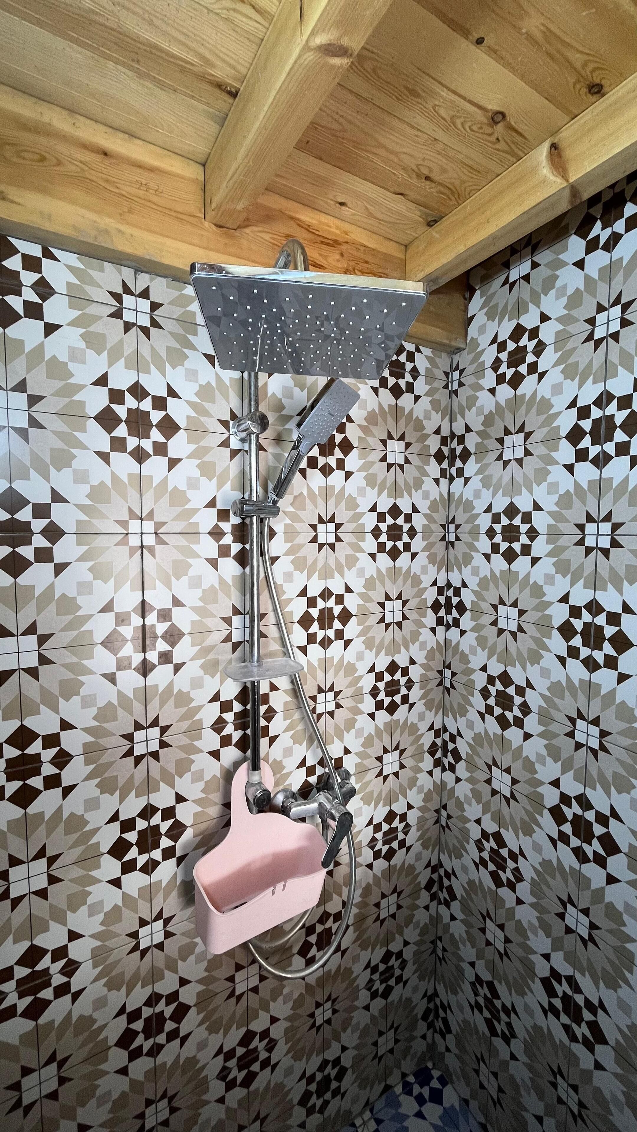 A shower with a geometric tile pattern on the walls and a wooden ceiling.