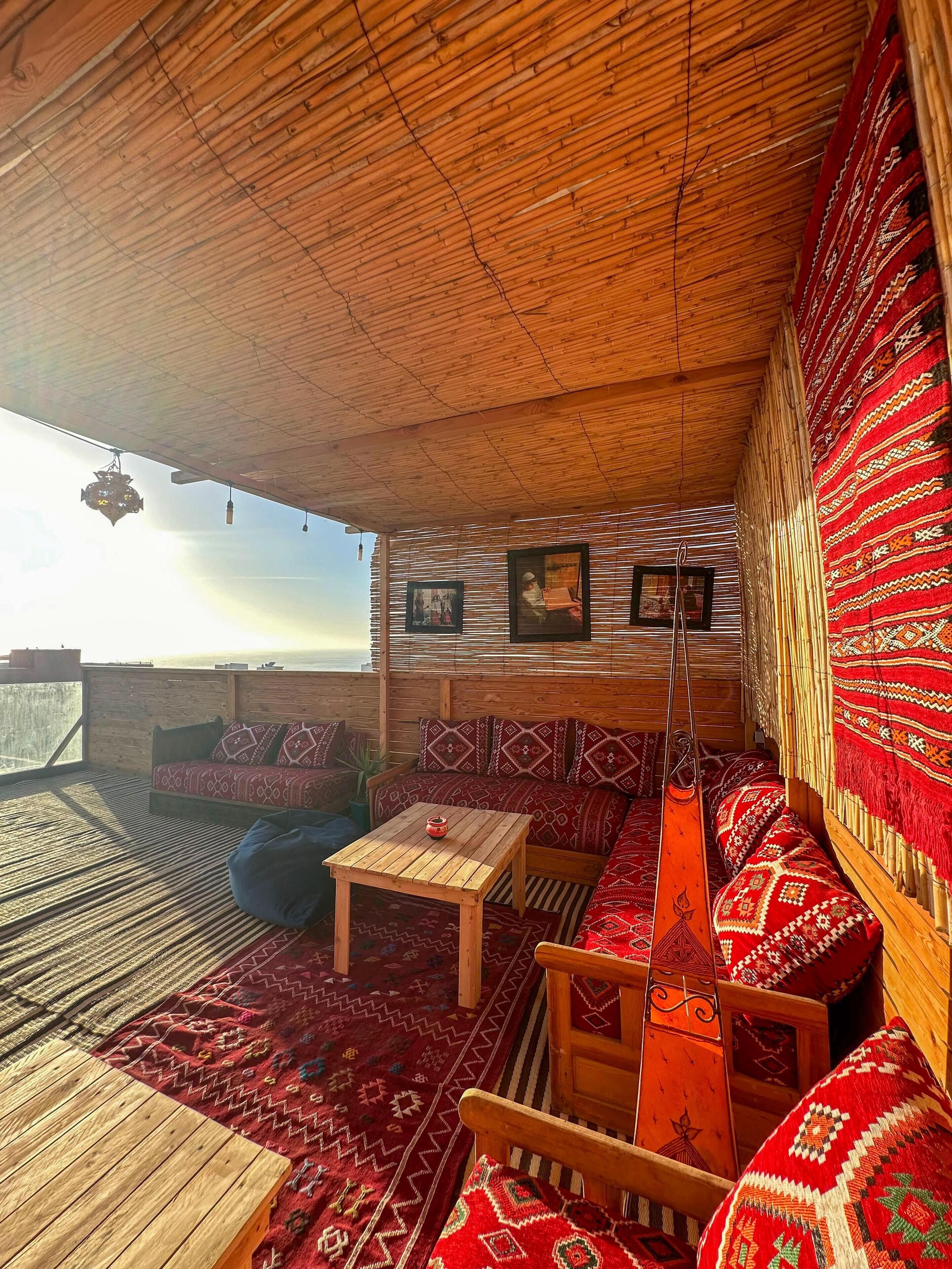 A cozy, wooden interior with a high ceiling, patterned cushions, and a view of the sky.