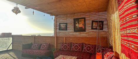 A cozy, wooden interior with a high ceiling, patterned cushions, and a view of the sky.