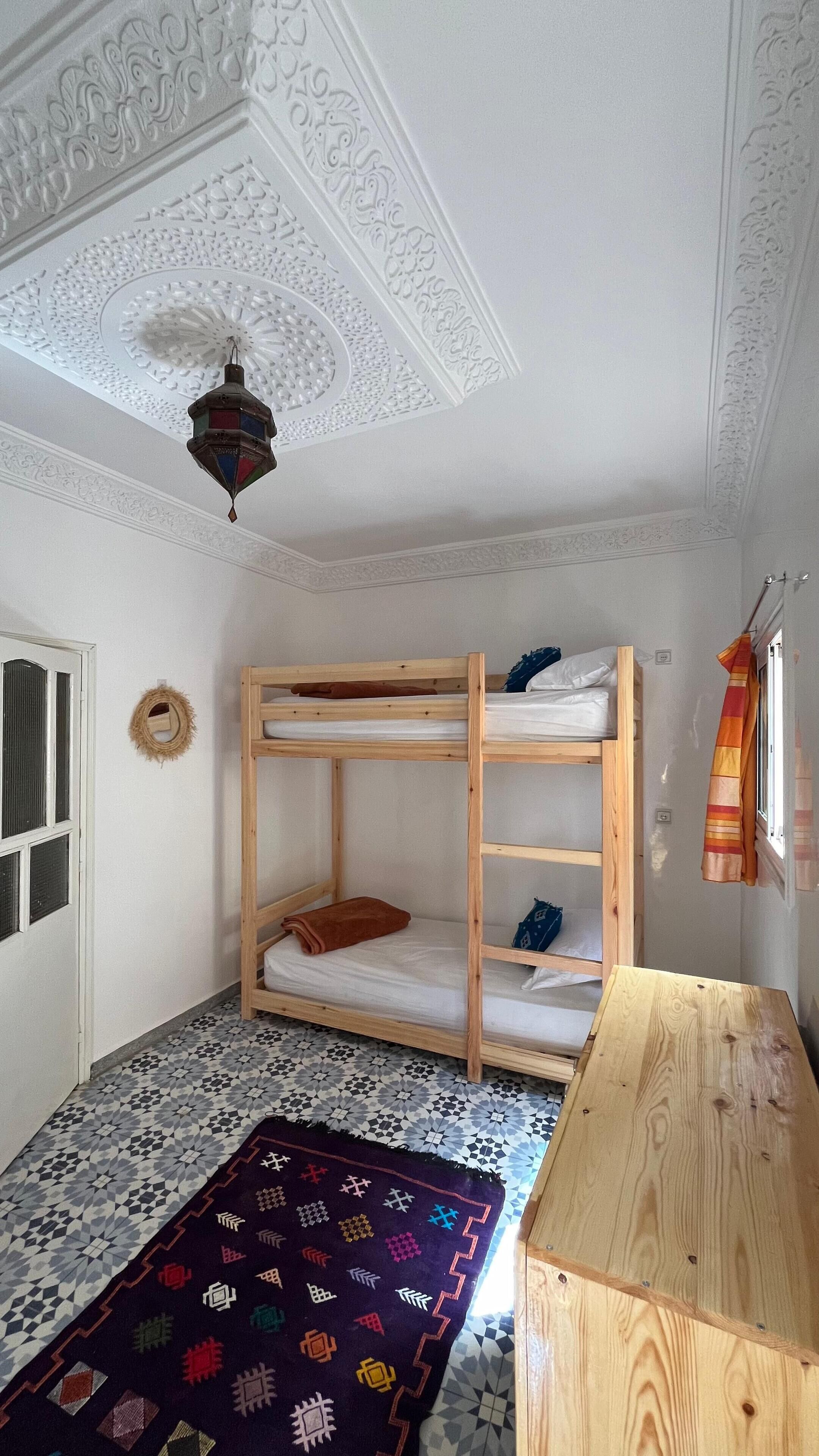 A room with a bunk bed, a patterned rug, and a wooden table.