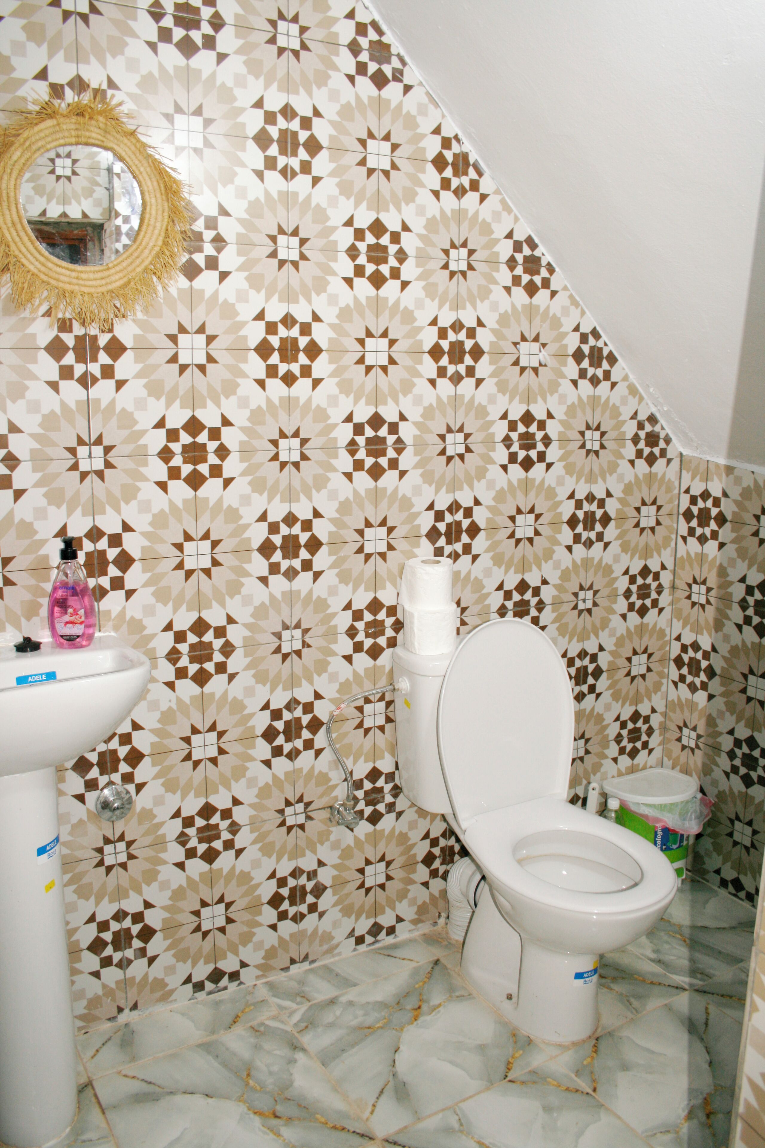 A bathroom with a geometric patterned tile wall, a white sink, and a toilet.