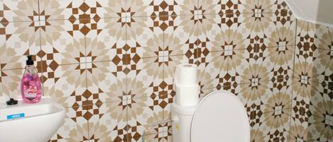 Un baño con pared de azulejos estampados geométricos, un lavamanos blanco y un inodoro.