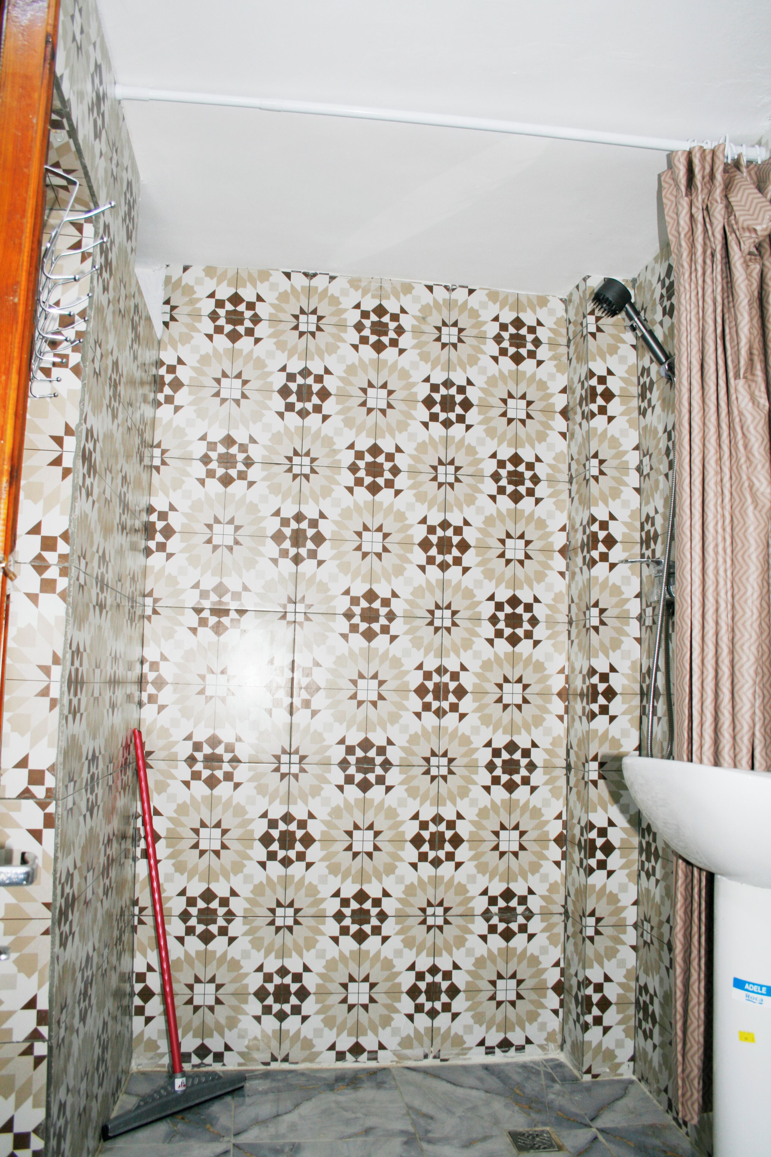 Un baño con baldosas estampadas, una cortina de ducha y una escoba roja.
