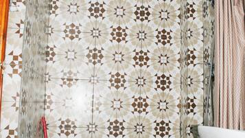 Une salle de bain avec des carreaux décorés, un rideau de douche et un balai rouge.