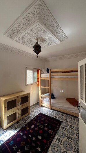 A room with a bunk bed, a wooden cabinet with drawers, a patterned rug, and a decorative ceiling. - Aourir Waves Surf House (Aourir)