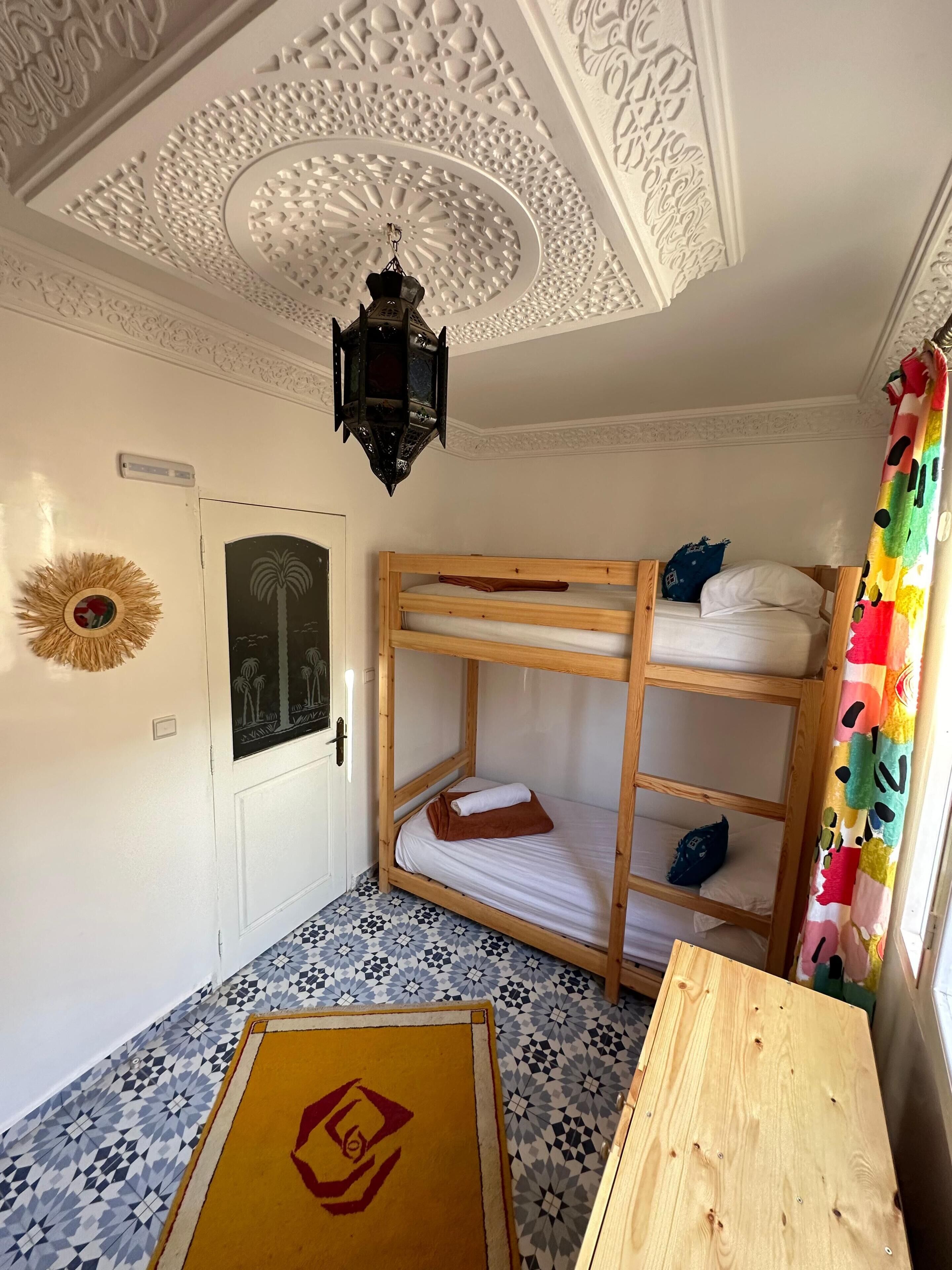 A room with a bunk bed, a patterned floor, a decorative ceiling, and a small table.