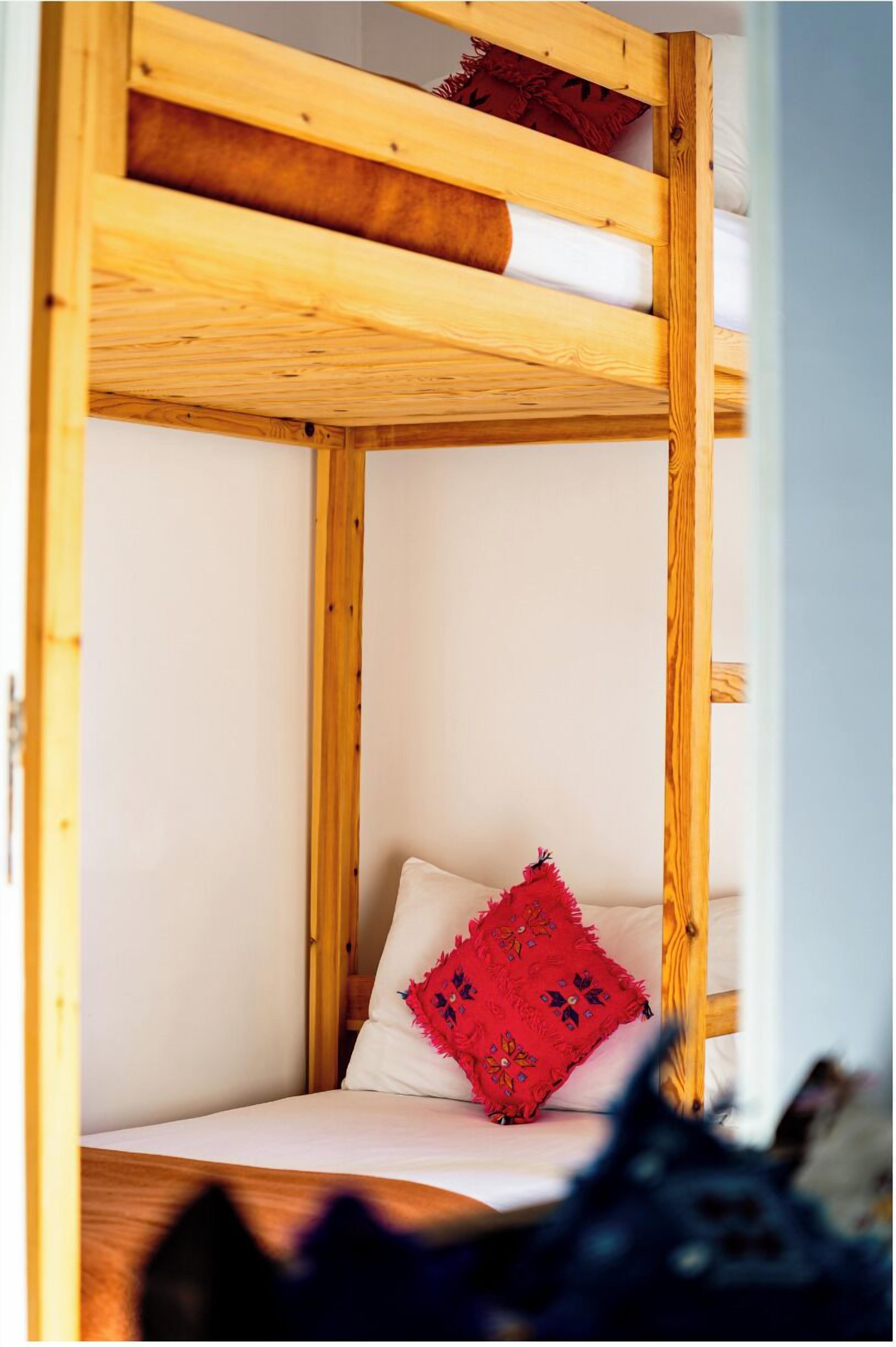 Una cama litera de madera con un cojín decorativo rojo y un cojín blanco.